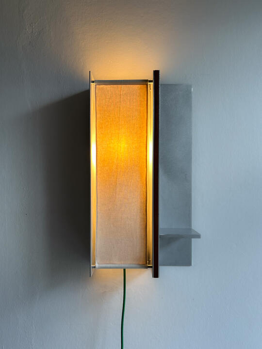 A wall lamp made of hand brushed aluminium with a strip of dark hardwood and a soft calico cover. Designed and made by Liam Barwick